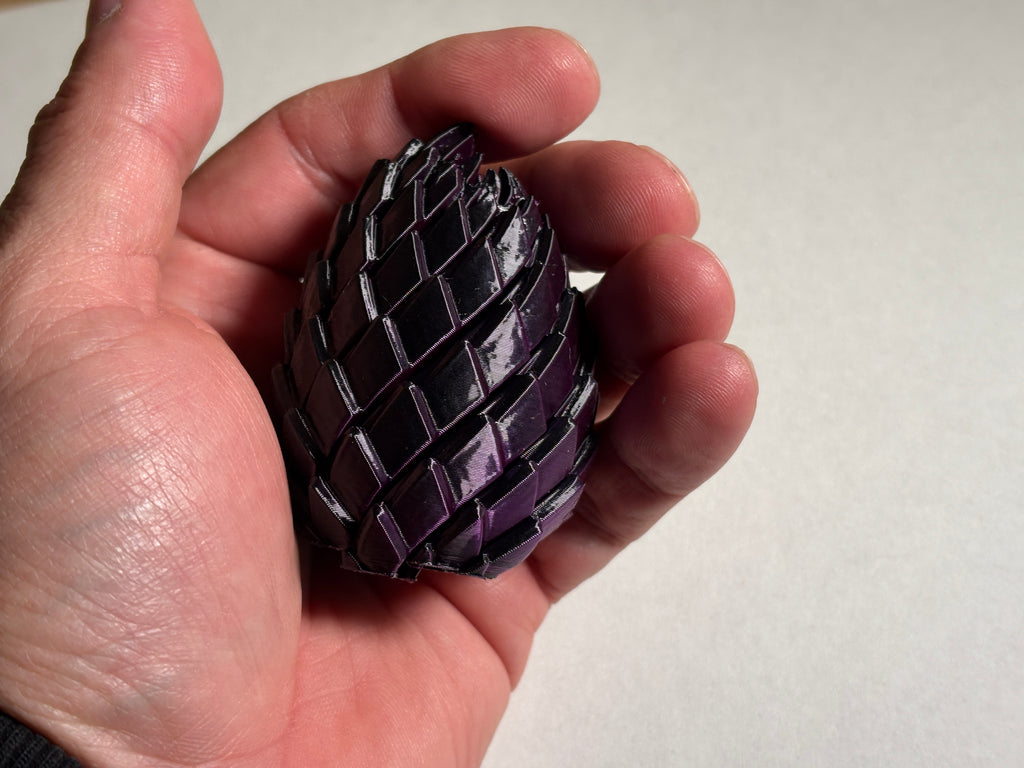 A hand holding a purple dragon egg fidge toy