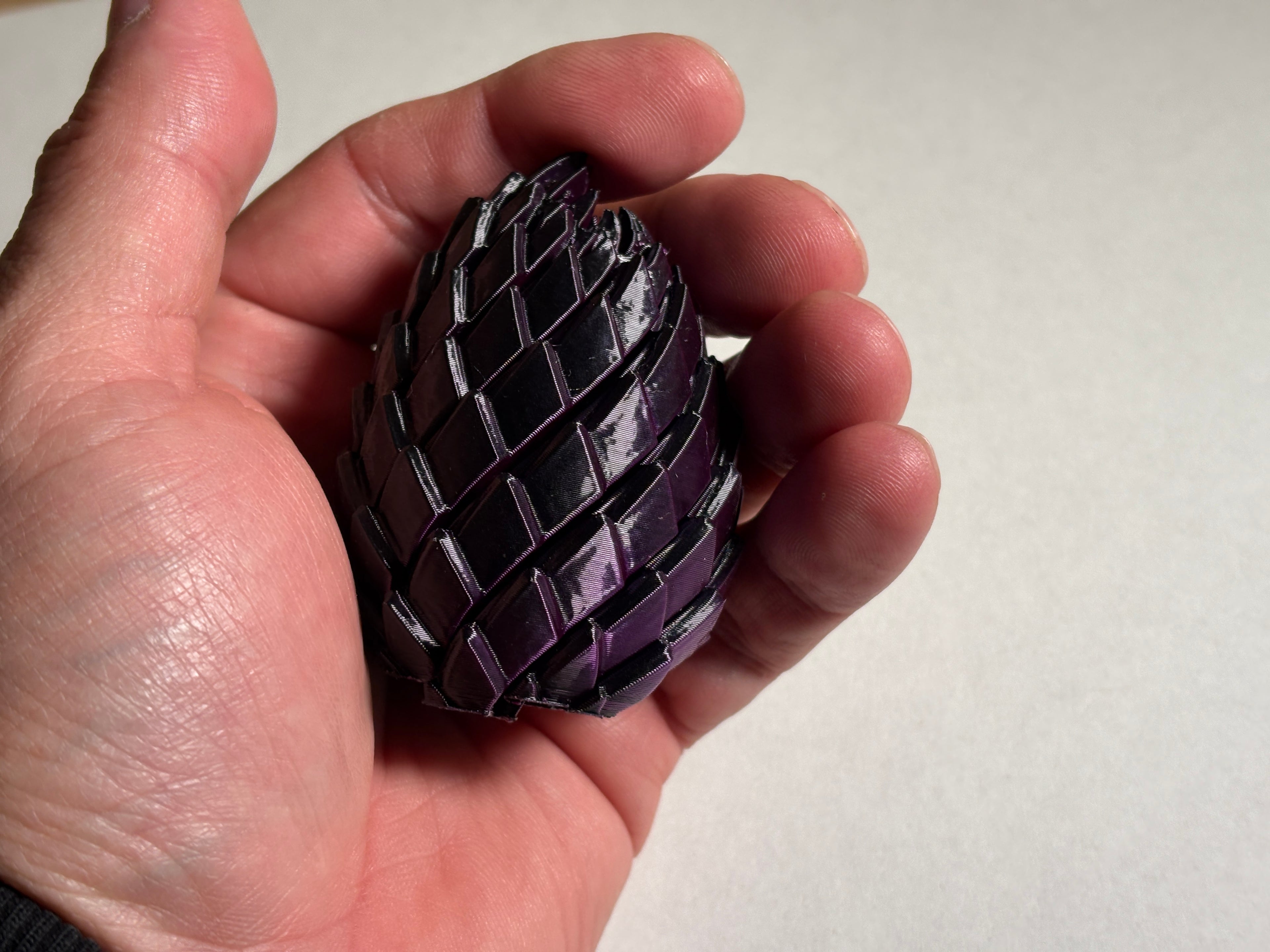 A hand holding a purple dragon egg fidge toy