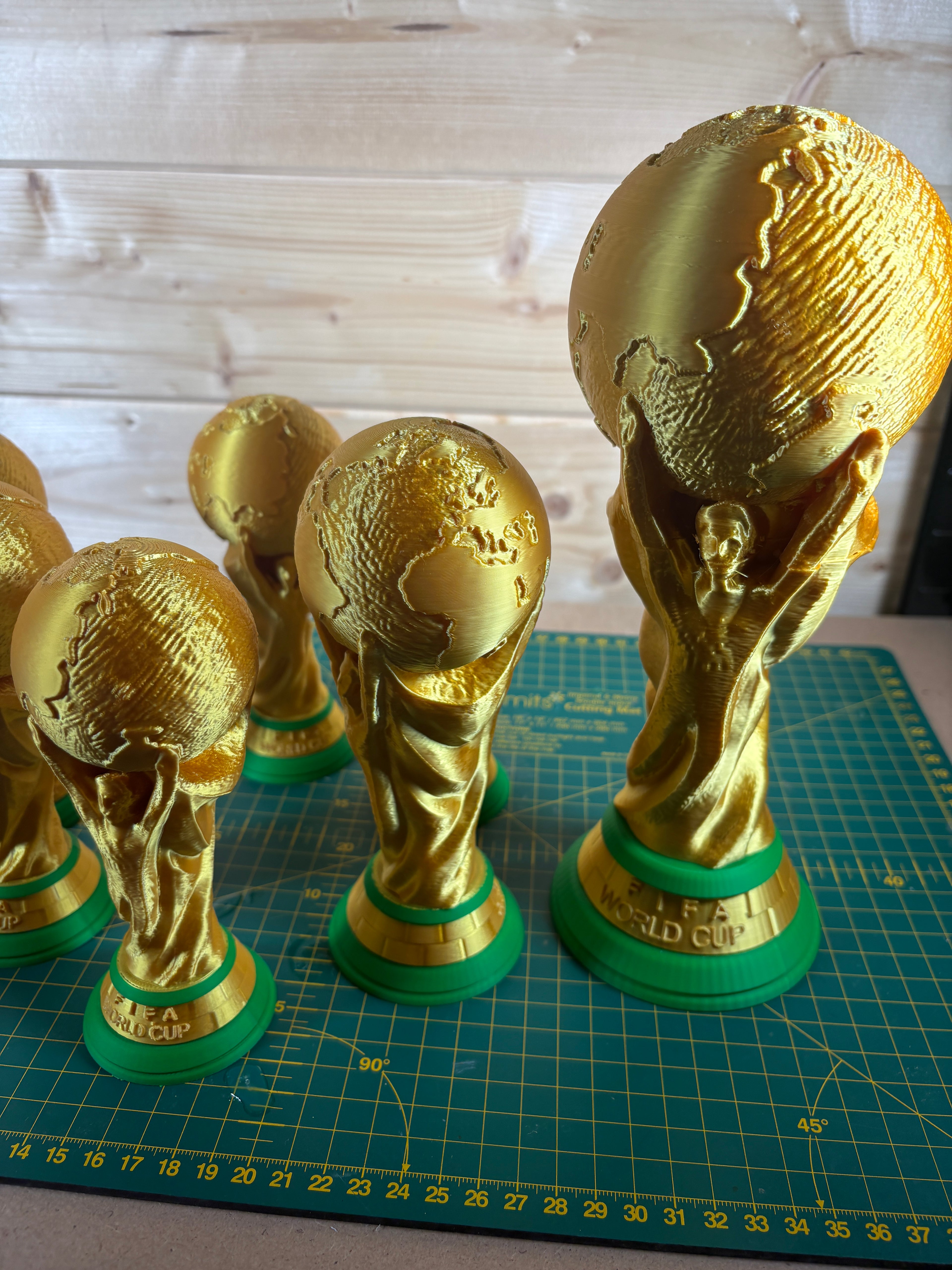 Gold and green World Cup trophies on a cutting mat with a wooden surface background
